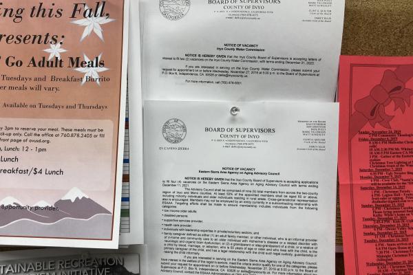 Bulletin board with flyers, including two advertising notices of vacancy for the Inyo County Water Commission and Eastern Sierra Area Agency on Aging Advisory Committee