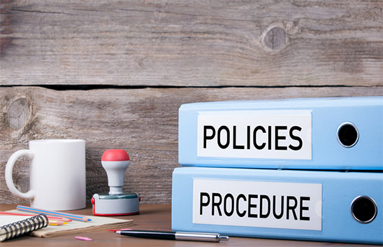 Binders labeled "Policies" and "Procedure" stacked on a wooden table