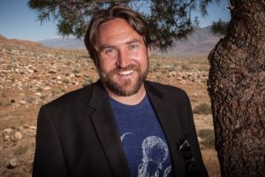 Man with beard wearing blue t-shirt and black blazer.