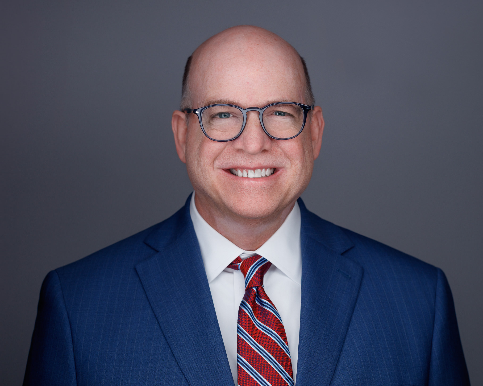 Bald man with glasses, white shirt, blue suit jacket