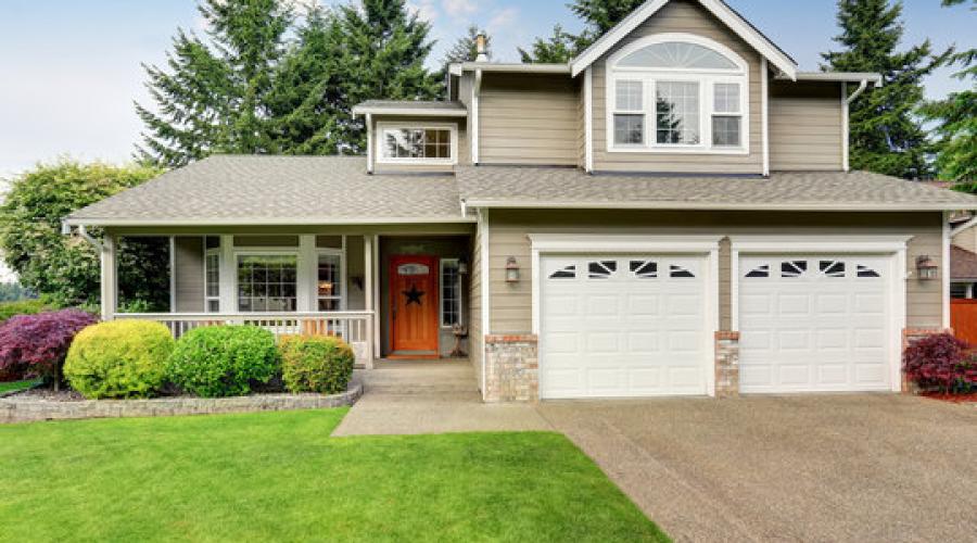 Beige house with double garage, driveway, and lawn.