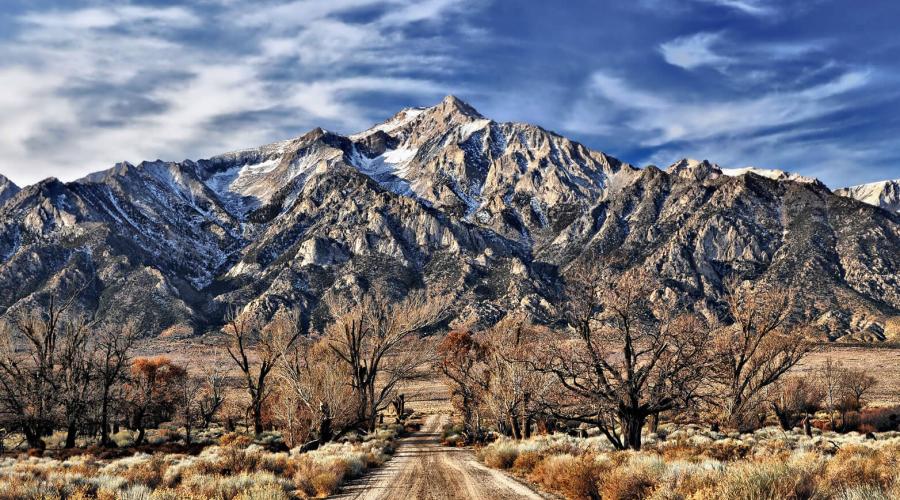 dirt road leading to large mountain with blue skies and white clouds