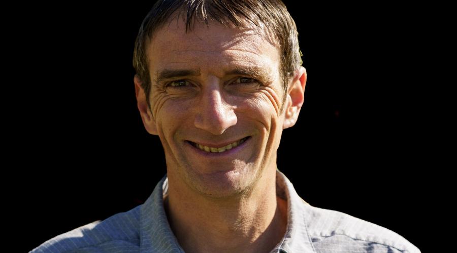 Man with blue shirt in front of black background.