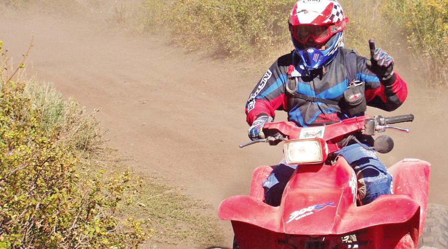 Individual dressed in motorcycle gear riding a red quad on a dirt road.