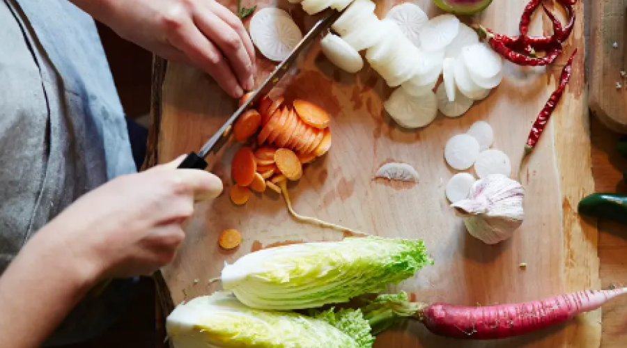 View looking down on a wooden cutting board as someone chops vegetables
