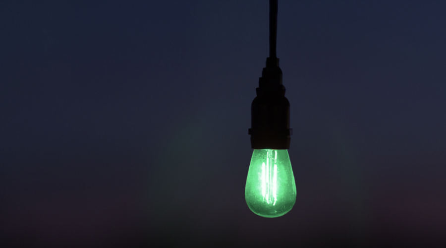 A cord hanging down in a dark area with an illuminated green light bulb hanging from it.