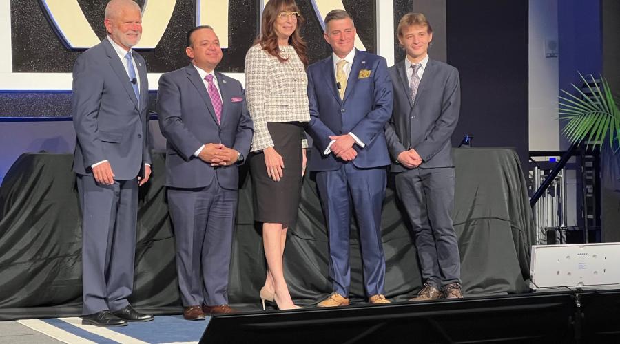 Two men, a woman, and two more men stand together on a stage.