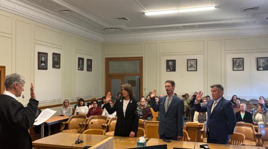 Robed judge swearing in three individuals.