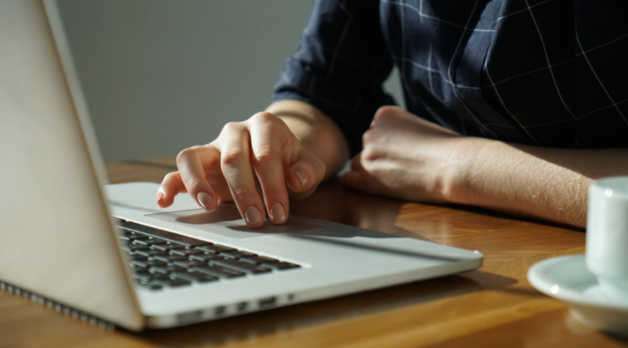 Man's arms shown in front of a laptop on a table, as if he is working on the computer.