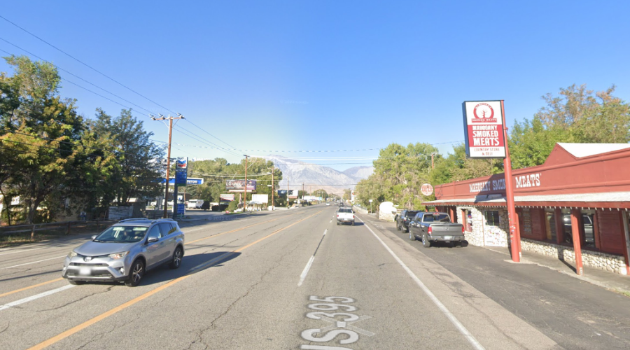 Highway as seen from the right lane, with a car coming toward the camera from the left lane, and a red barn-like building is on the right.