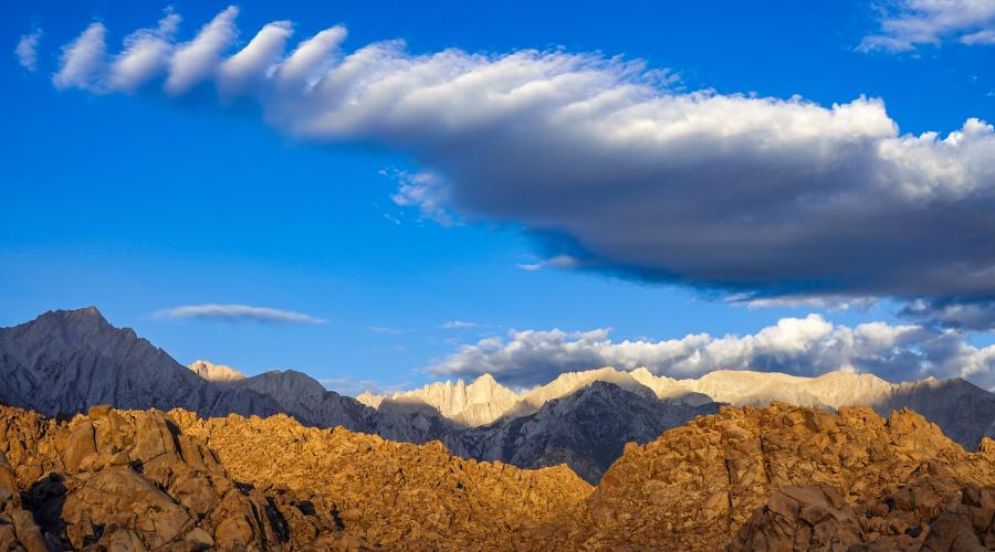 Brown foothills in the Alabama Hills with the Sierra and Mt. Whitney looming in the background under a bright blue sky with a Sierra Wave.
