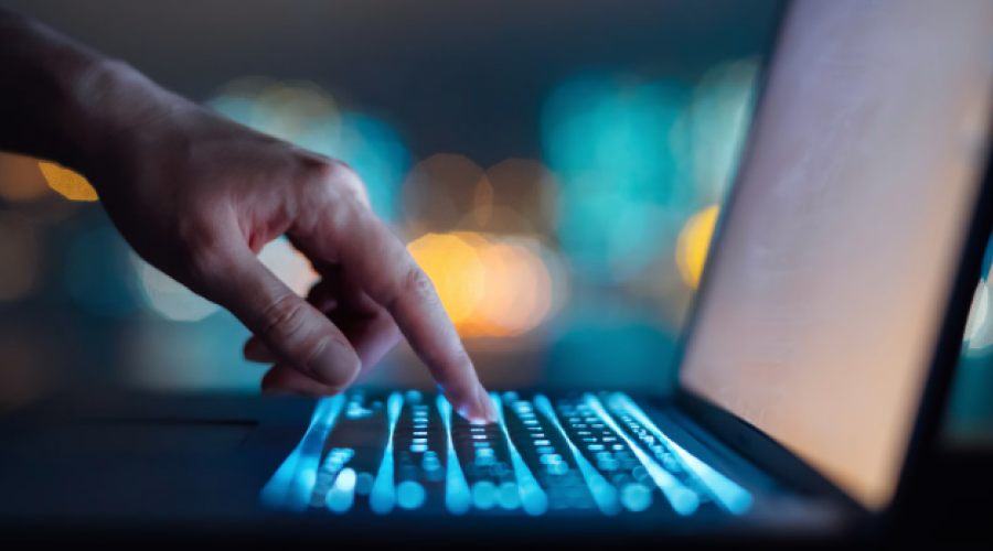 Male arm with finger touching back-lit keyboard of laptop 