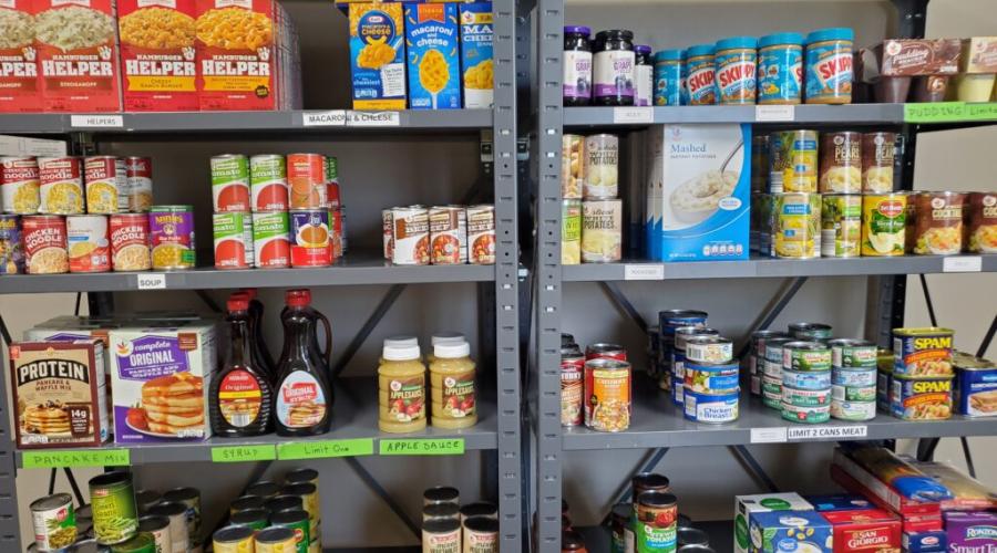 Metal shelves stocked with items like peanut butter, jelly, macaroni.