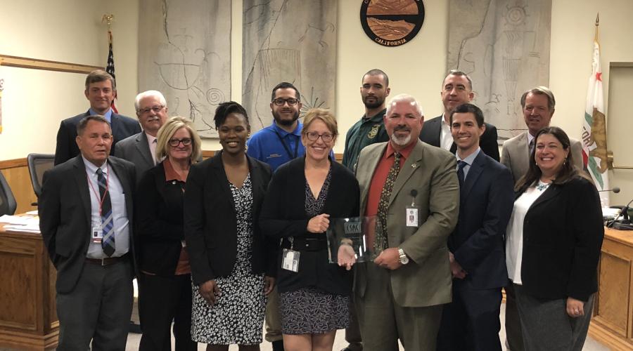 Group of men and women standing in front of wooden dais in Board of Supervisors chambers