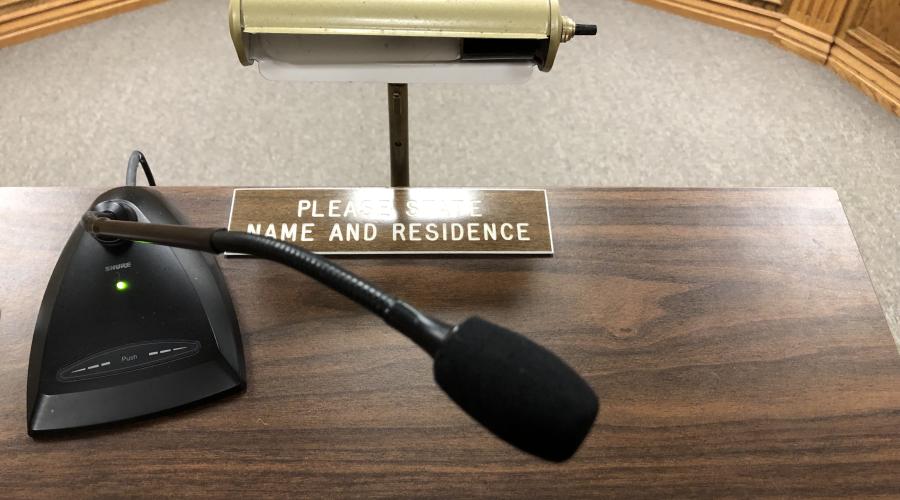 Microphone on top of speaker podium with lamp and sign stating: "Please State Name and Residence" 