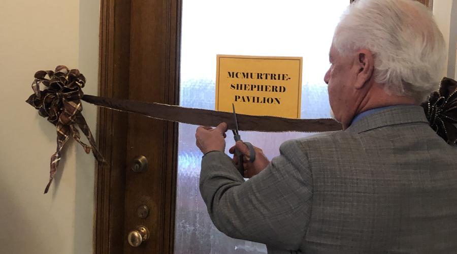 Man uses scissors to cut ribbon strung across doorway