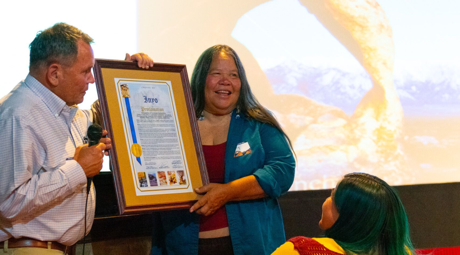 Man with microphone looks at framed proclamation being held by woman standing next to him