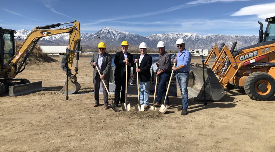 Five men wearing hard hats and holding shovels near construction equipment.