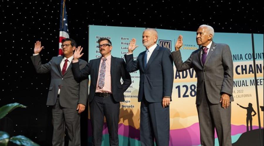 Four men in suits taking an oath of office on a stage.