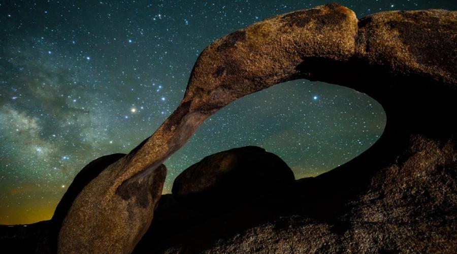 Rock arch formation with starry night sky in background.