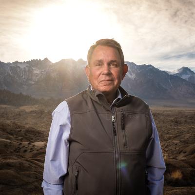 Man in Dress Shirt and Vest Standing in Front of Mountain Range At Dusk