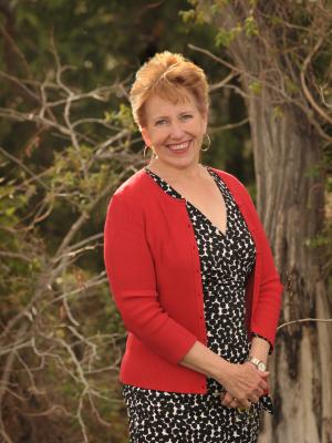 Woman with black dress and red sweater in front of trees
