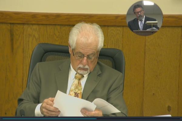 Chairperson Pucci reading papers with CAO Quilter's image displayed in corner